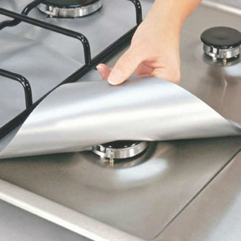 Hand peeling off silver protective stove burner cover on stainless steel gas cooktop